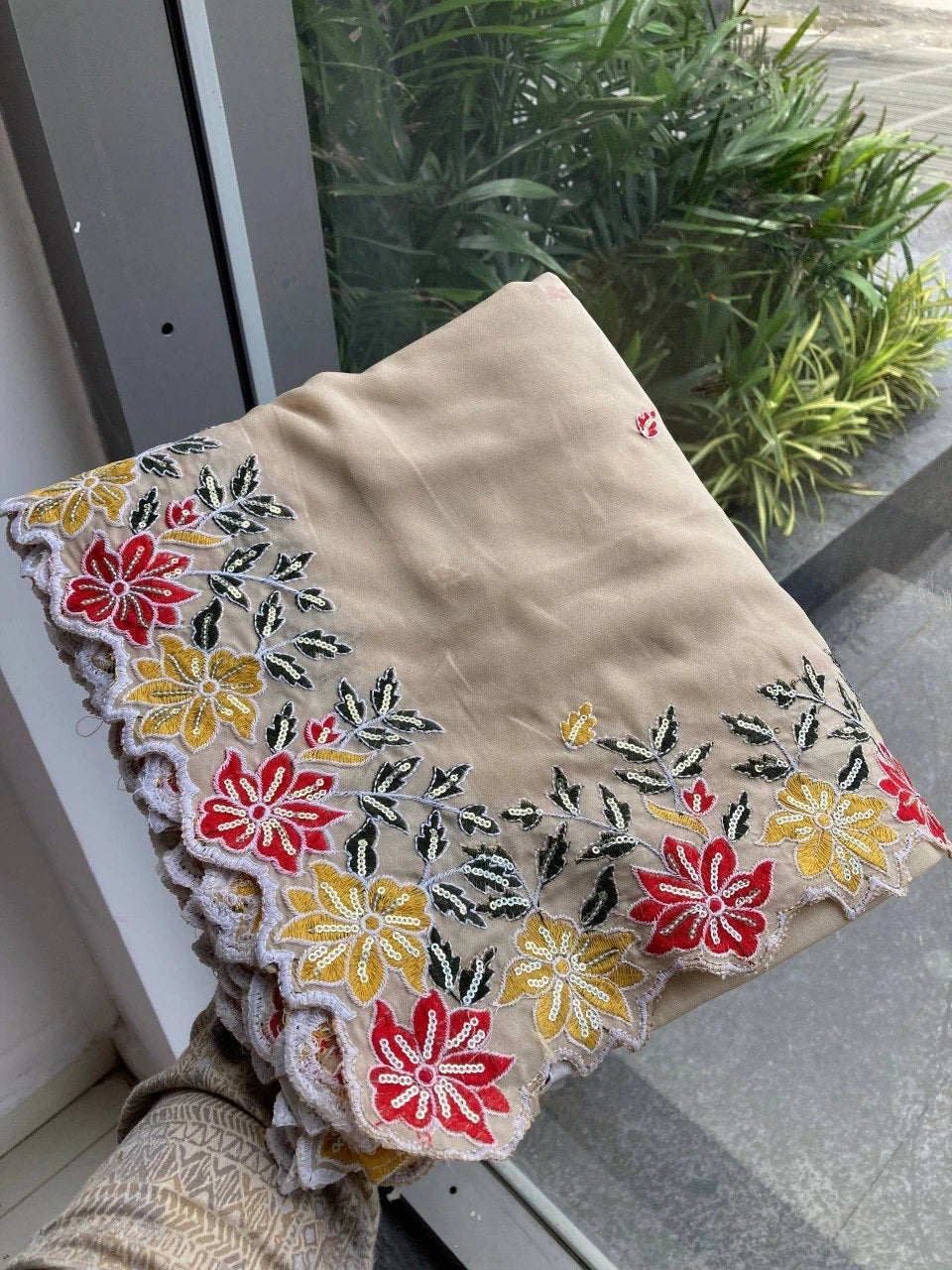 Beige fabric with floral embroidery held by a person outdoors.